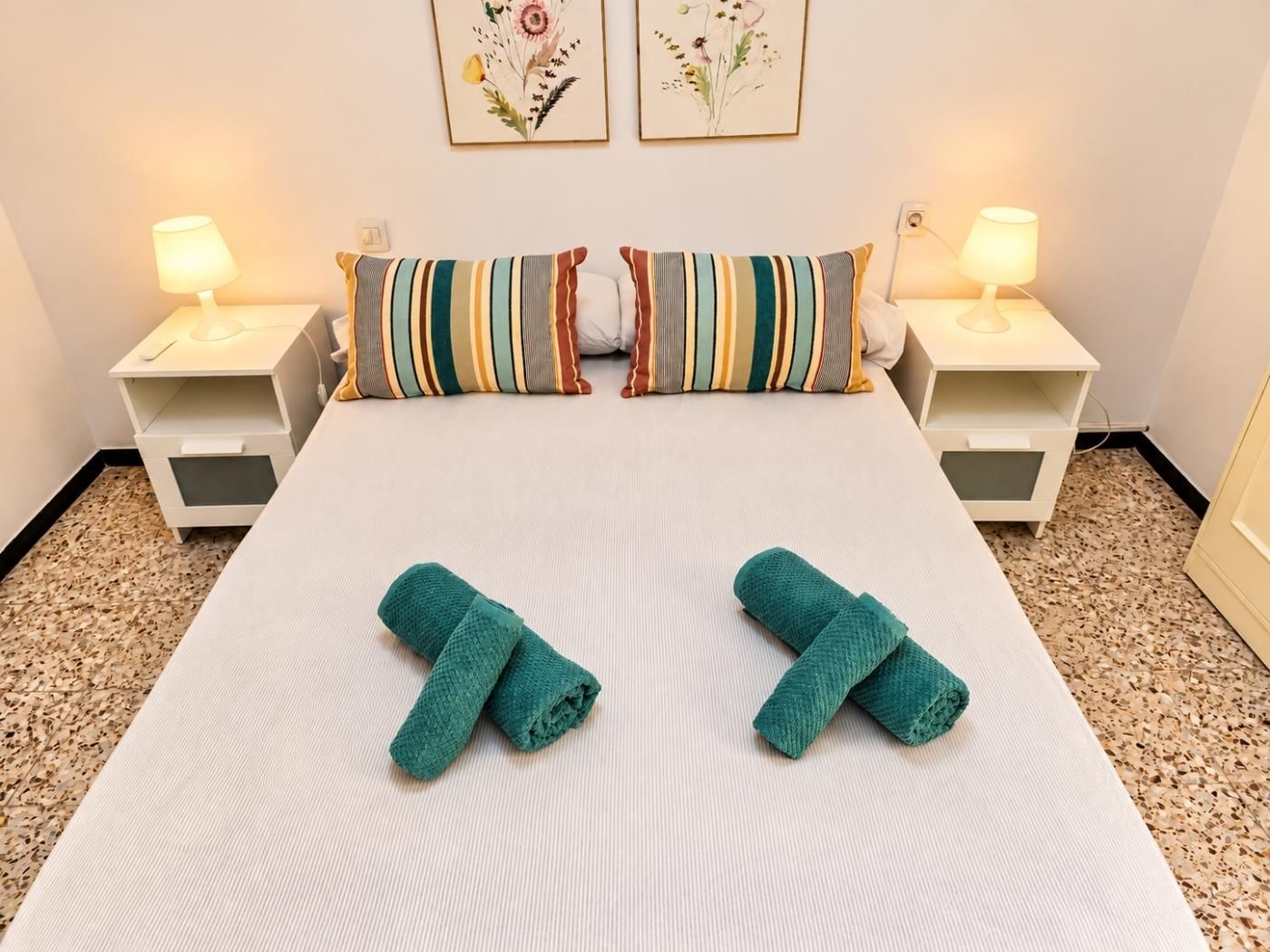 Ein ordentlich gemachtes Bett mit gestreiften Kissen, zwei Nachttischlampen und zwei gefaltete Handtücher auf dem Bett.