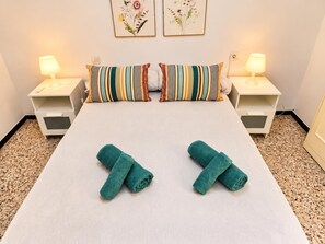 Ein ordentlich gemachtes Bett mit gestreiften Kissen, zwei Nachttischlampen und zwei gefaltete Handtücher auf dem Bett.