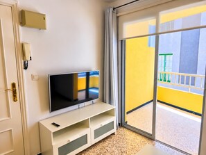A room with a flat-screen TV on a white stand, a telephone, and a sliding glass door leading to a balcony with yellow walls. - One bedroom, balcony, Wi-Fi, El Médano centre (El Médano)
