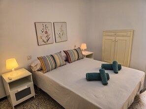 A neatly arranged bedroom with a bed, pillows, a nightstand, a lamp, a wardrobe, and two wall-mounted floral artwork pieces. - One bedroom, balcony, Wi-Fi, El Médano centre (El Médano)