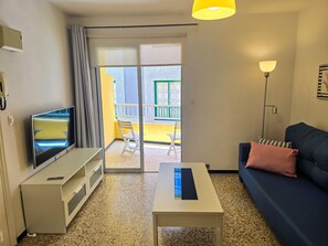 A living room with a TV, a sofa, a coffee table, a balcony with a chair, and a lamp. - One bedroom, balcony, Wi-Fi, El Médano centre (El Médano)