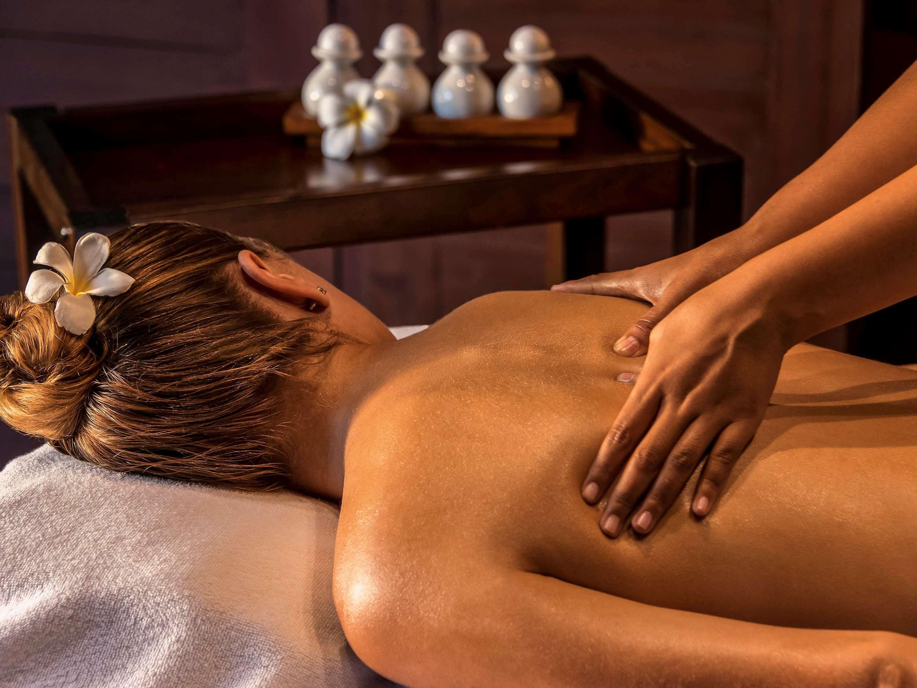 A person receiving a back massage in a room with a wooden table and salt lamps in the background.