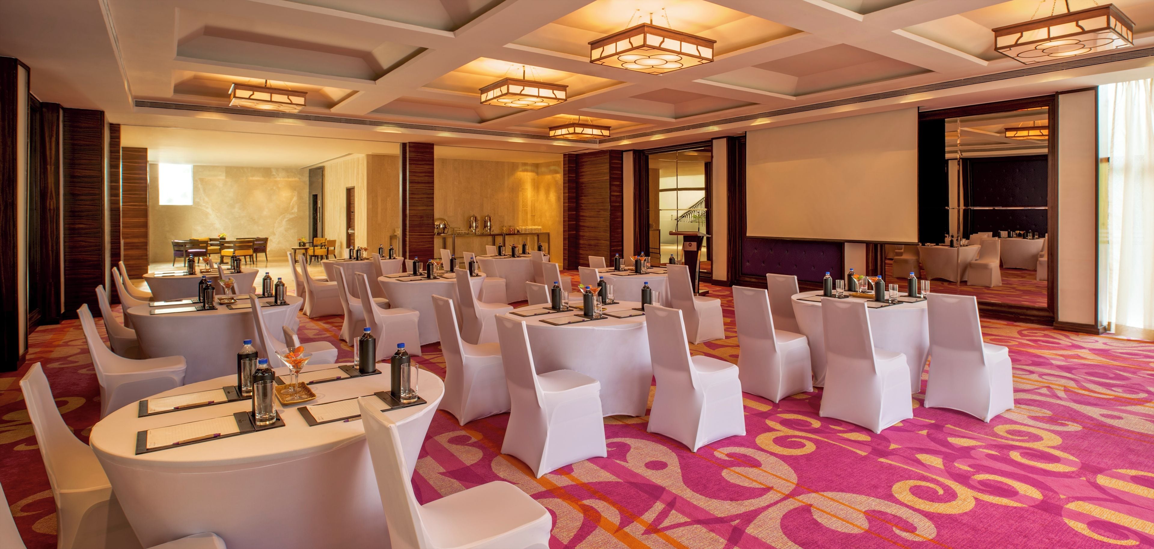 A conference room with round tables, white chairs, and a large screen.