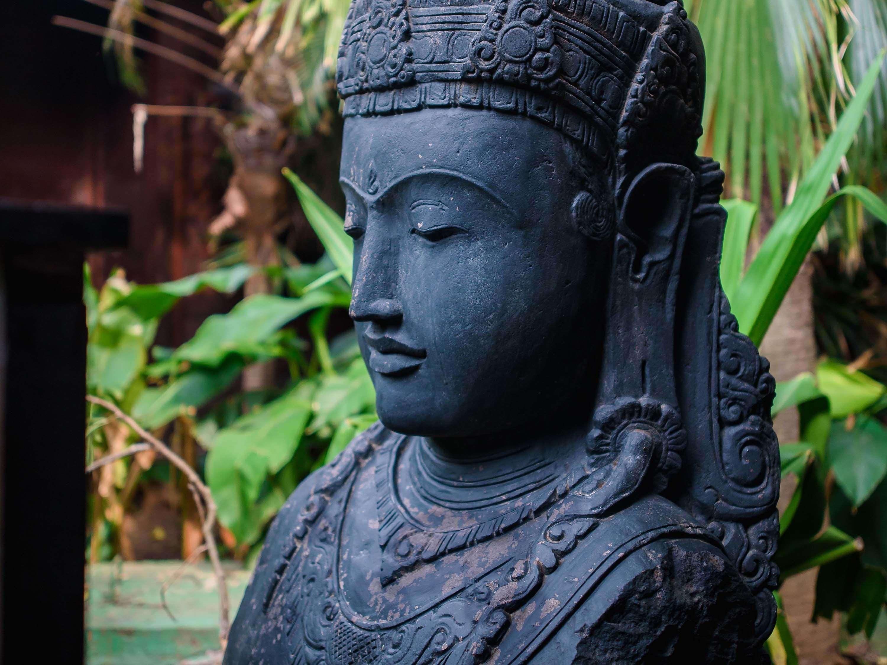A statue with intricate carvings, set against a backdrop of greenery.