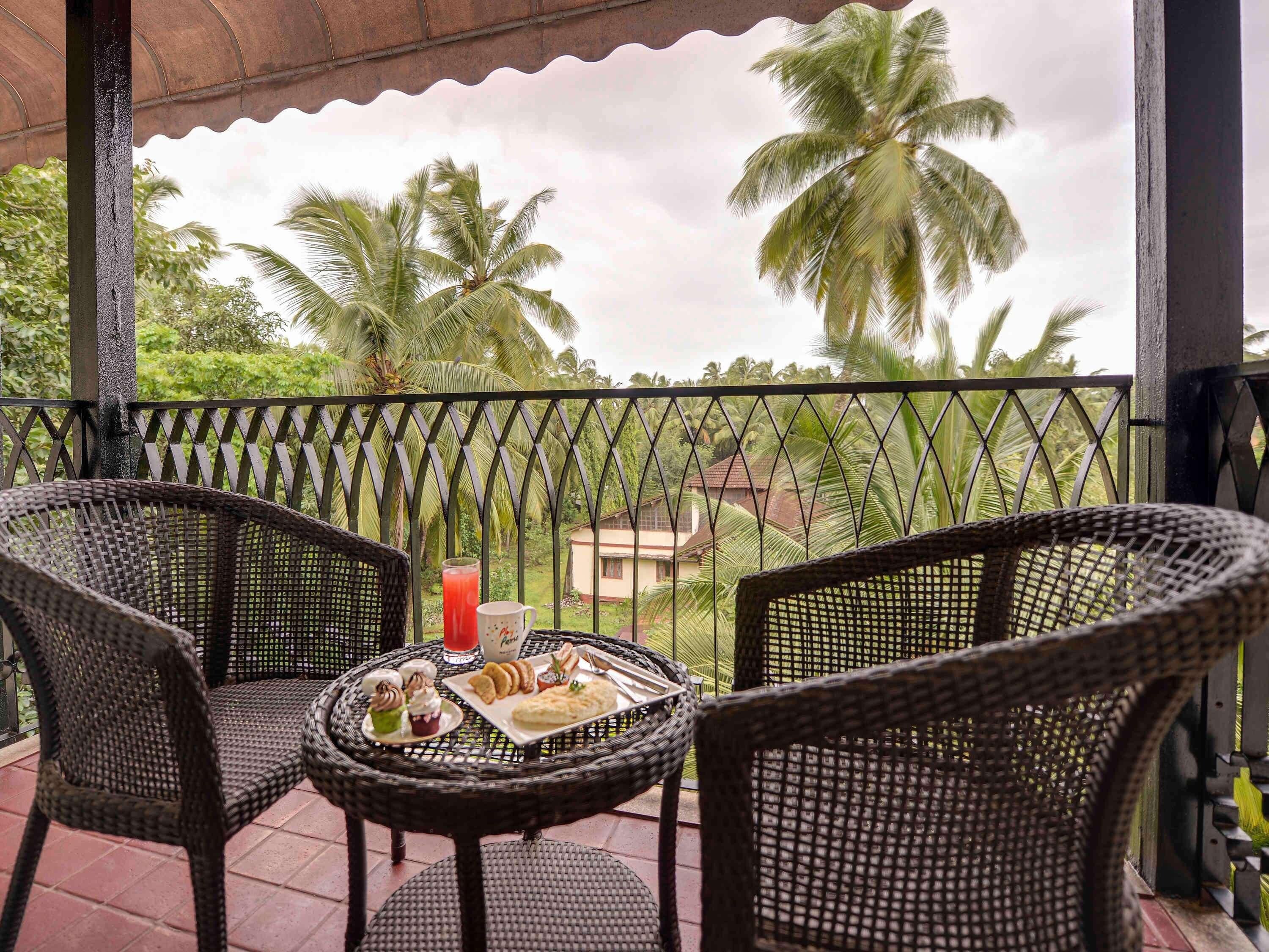 A balcony with wicker chairs and a table, a drink, and a plate of food.