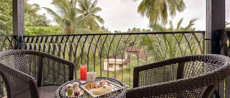 A balcony with wicker chairs and a table, a drink, and a plate of food.