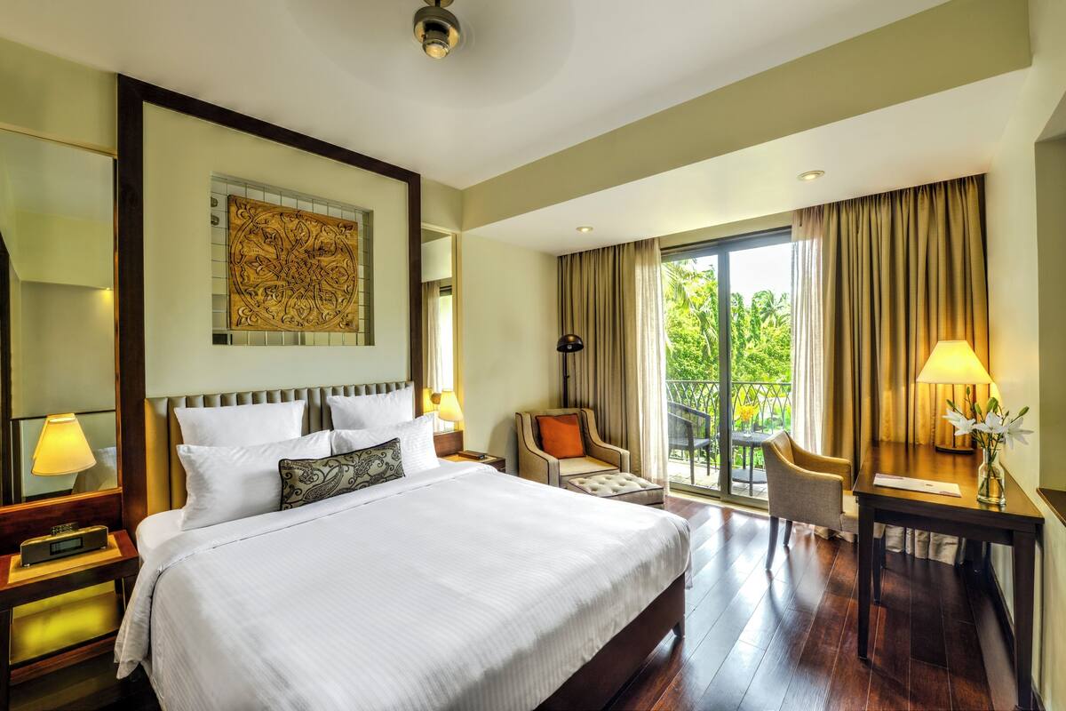 A hotel room with a large bed, a desk, a chair, and a balcony with a view.