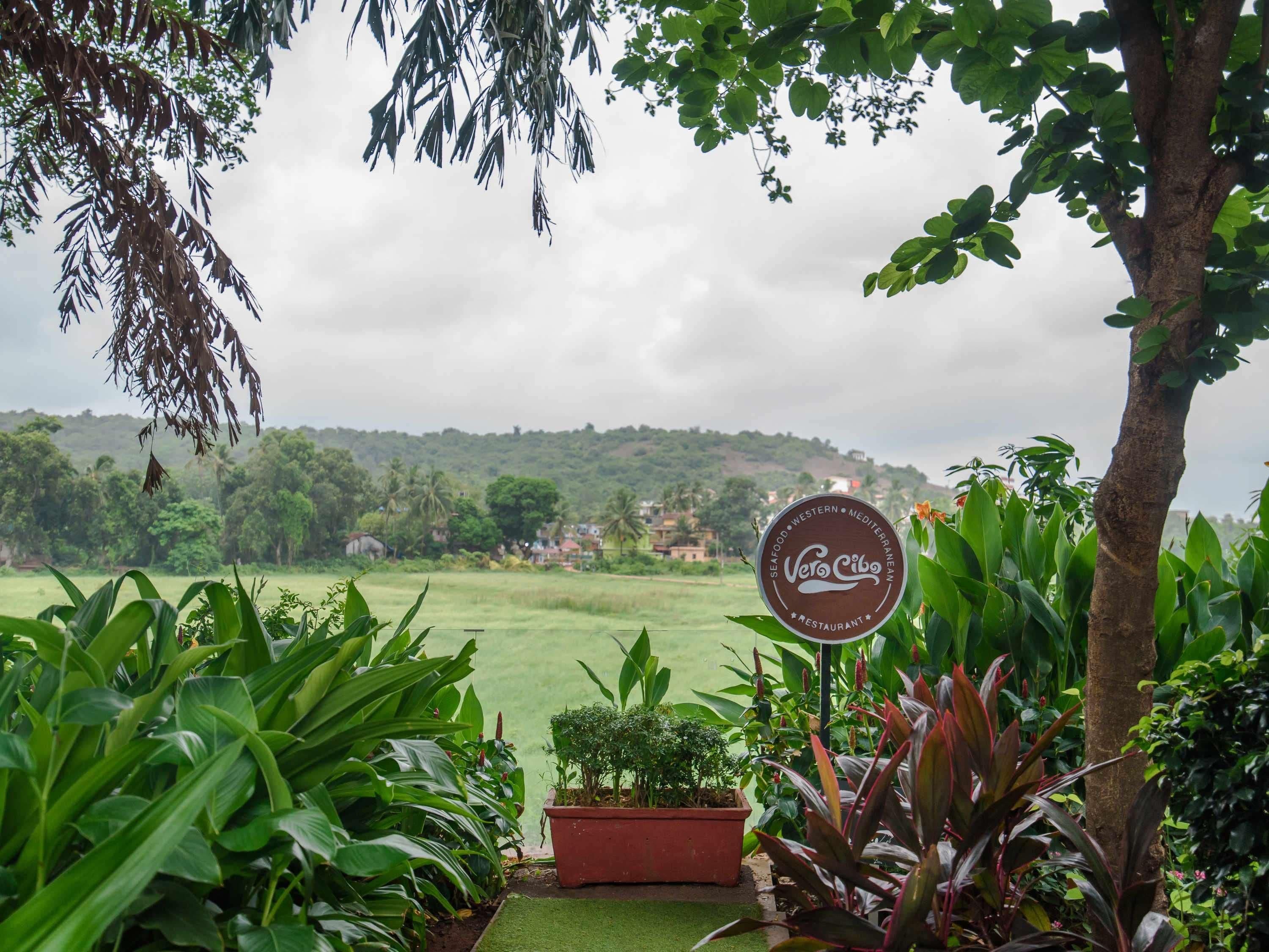 A sign for 'Vero Cibo' restaurant with a view of a green field and trees.