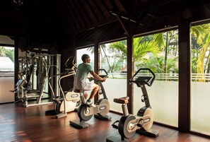 Un gimnasio con equipo de ejercicio y amplias ventanas con vistas a un paisaje tropical.