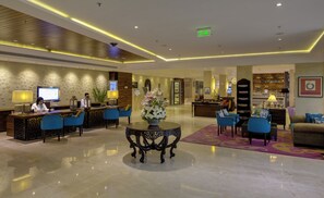 Un hall de hotel con mostrador de recepción, zona de estar y bar.