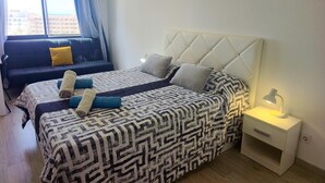 Ein Schlafzimmer mit Bett, Vorhängen am Fenster, einer Couch und einem Nachttisch mit Lampe.
