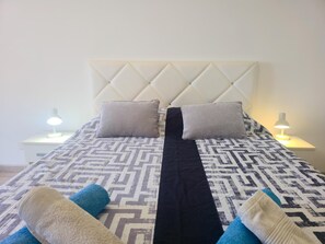 Een bed met een beddegoed met patroon, twee kussens en twee nachtlampjes.