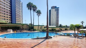 Ein Hotelpoolbereich mit mehreren Schwimmbecken, Palmen und Hochhäusern im Hintergrund.
