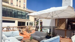 Eine Dachterrasse mit Außenbestuhlung, einem großen Sonnenschirm und Blick auf ein Gebäude mit einem weißen Turm.