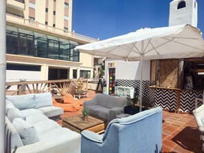 A rooftop terrace with outdoor seating, a large umbrella, and a view of a building with a white tower. - One bedroom, Balcony, WI-FI, Pool,600 meters from the Sea (Playa Paraiso)