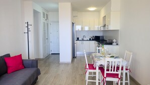 Ein kompakter Wohnraum mit Essbereich, Küchenzeile und einem grauen Sofa mit roten Kissen.