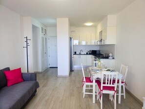A compact living space with a dining area, kitchenette, and a grey sofa with red cushions. - One bedroom, Balcony, WI-FI, Pool,600 meters from the Sea (Playa Paraiso)
