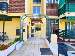 A building entrance with a gated entrance, a sign indicating a private road, and a small outdoor seating area with a trash bin. - 3 bedrooms, swimming pool, parking, 100 metres from the sea, Wi-Fi (Los Cristianos)