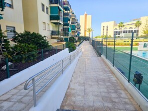 A pathway leading to a swimming pool with a fence, surrounded by buildings with balconies and a clear sky. - 3 bedrooms, swimming pool, parking, 100 metres from the sea, Wi-Fi (Los Cristianos)