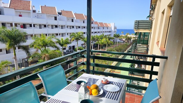 Een balkon met een tafel gedekt voor twee, met uitzicht op een woongebied met palmbomen en de zee.