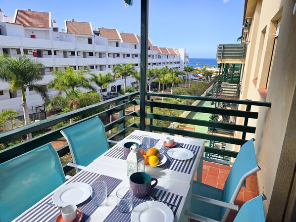 A balcony with a table set for two, overlooking a residential area with palm trees and a view of the sea. - 3 bedrooms, swimming pool, parking, 100 metres from the sea, Wi-Fi (Los Cristianos)