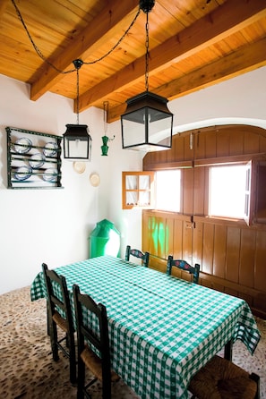A dining area with a checkered tablecloth, wooden chairs, a hanging lantern, and a window with wooden shutters. - Casas De Romaria (Mora)