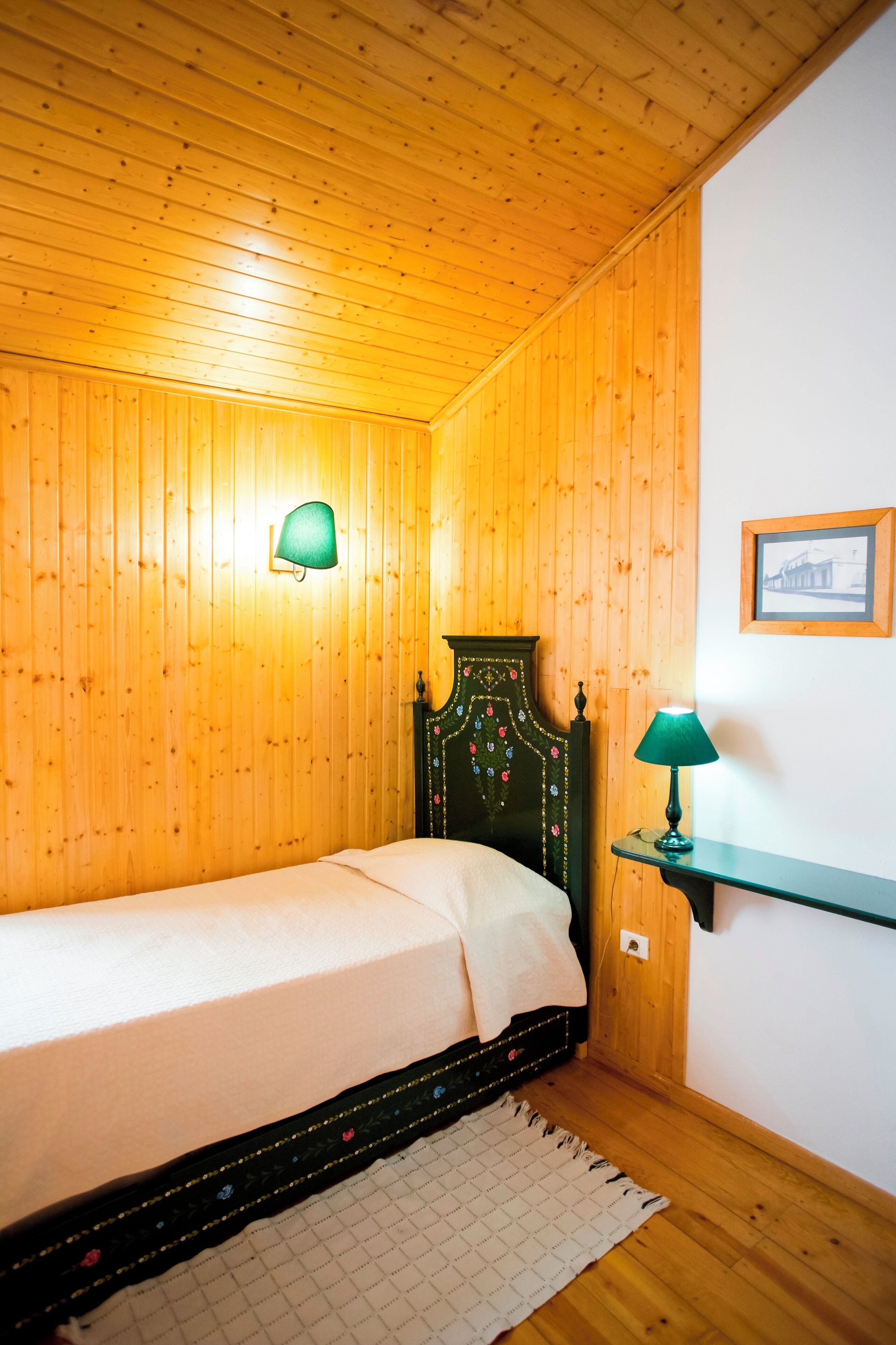Un llit individual amb capçalera verda en una habitació amb parets i sostre de fusta.