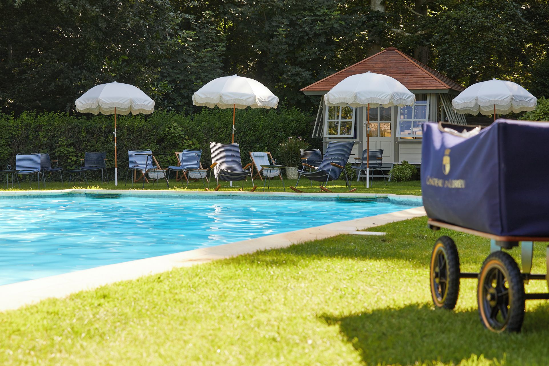 A swimming pool with lounge chairs and umbrellas, a small building, and a golf cart.