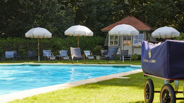 Una piscina con sillas de descanso y sombrillas, un edificio pequeño y un carrito de golf.