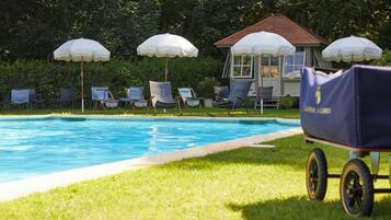 A swimming pool with lounge chairs and umbrellas, a small building, and a golf cart.