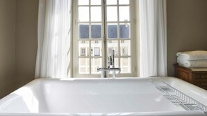 Una bañera grande y blanca en un baño con vistas a edificios a través de una ventana.
