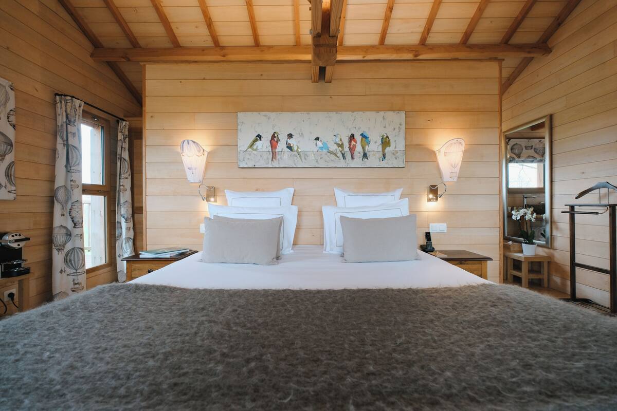 Quarto de cabana de madeira com uma cama grande, duas mesas de cabeceira, um quadro na parede e um espelho.