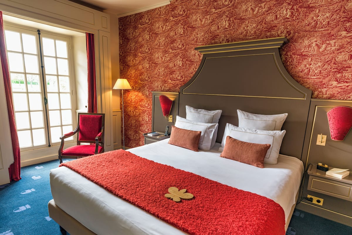 Quarto de hotel com uma cama grande, uma cadeira vermelha e parede com padrão.