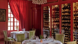 Comedor con mesas dispuestas para una comida, una estantería para vinos al fondo y una cortina roja.