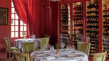 A dining area with tables set for a meal, a wine rack in the background, and a red curtain.