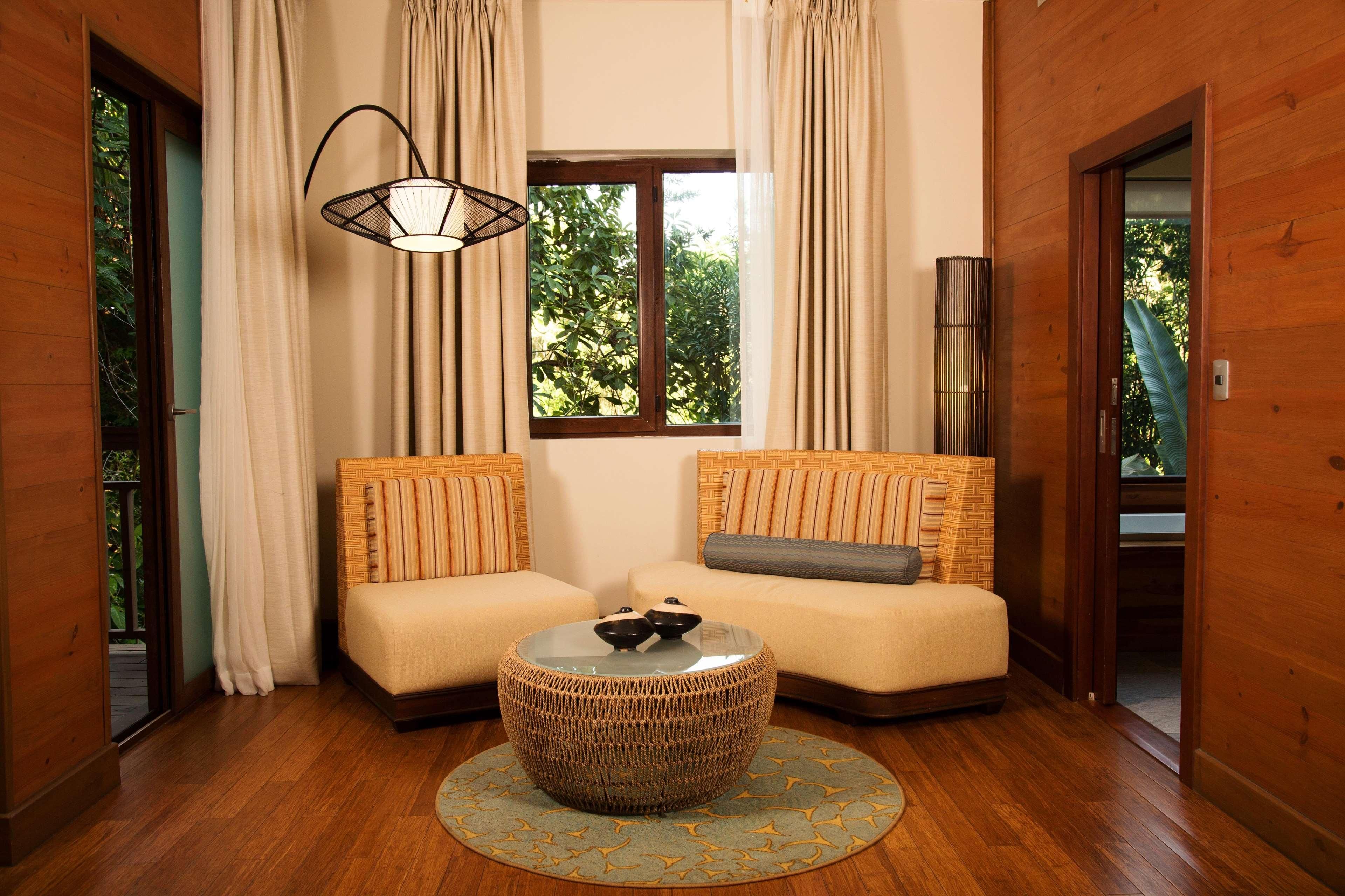 A room with two sofas, a round woven coffee table, a hanging light fixture, and a window with curtains.