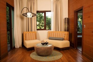 A room with two sofas, a round woven coffee table, a hanging light fixture, and a window with curtains. - Indura Beach & Golf Resort, Curio Collection (Tela)