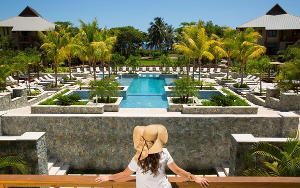 A resort with a central pool, lounge chairs, and palm trees.