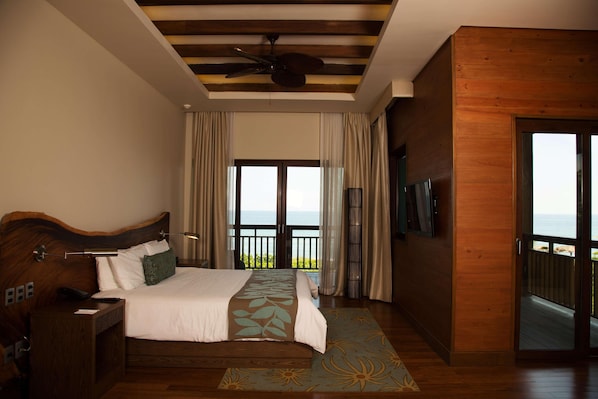 A bedroom with a bed, a nightstand, a telephone, a television, and a balcony with a view.