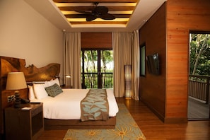 A hotel room with a bed, a ceiling fan, a TV, and a balcony with a view of trees. - Indura Beach & Golf Resort, Curio Collection (Tela)