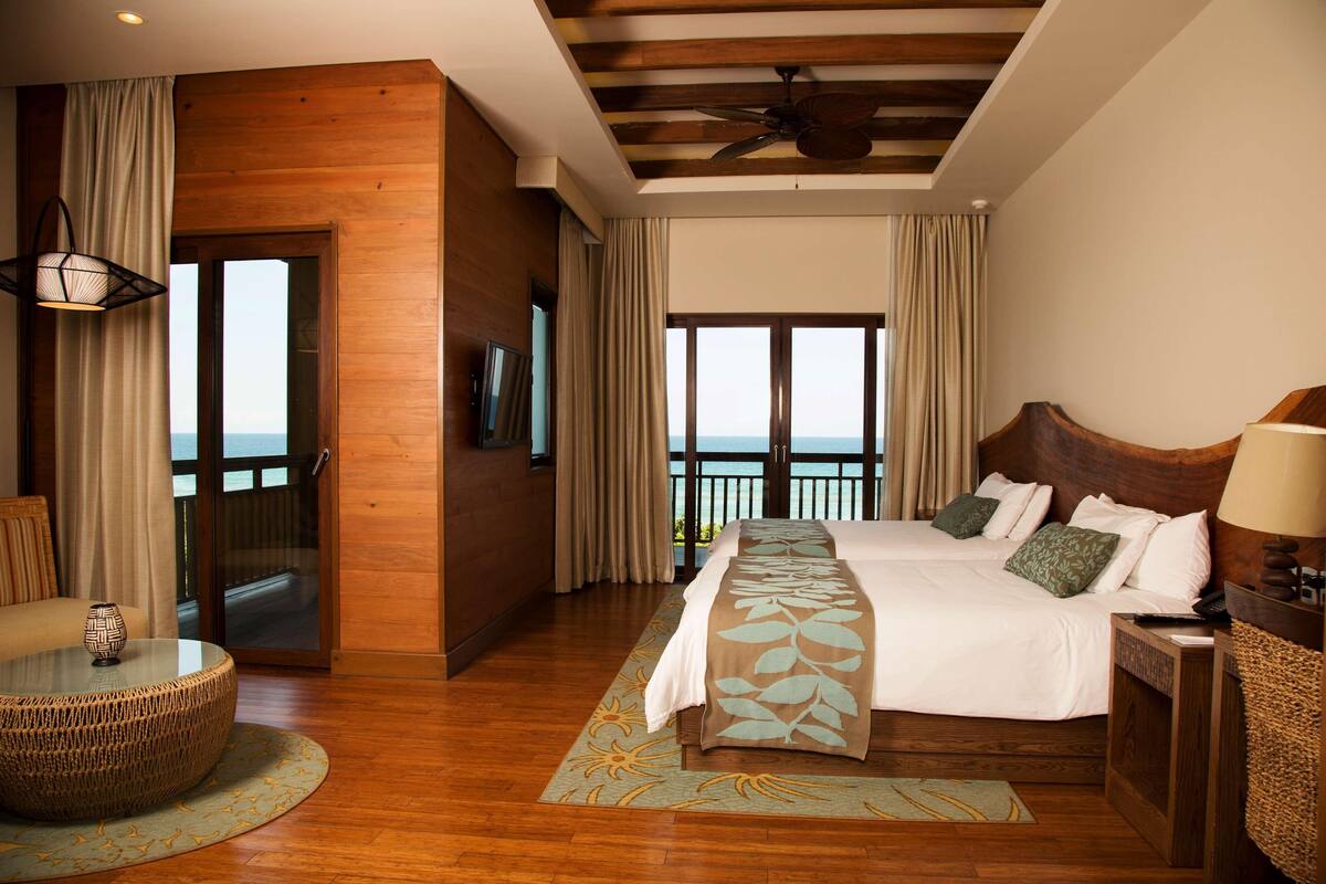 Un dormitorio amplio con una cama grande, un balcón con vistas, suelo de madera y un ventilador de techo.
