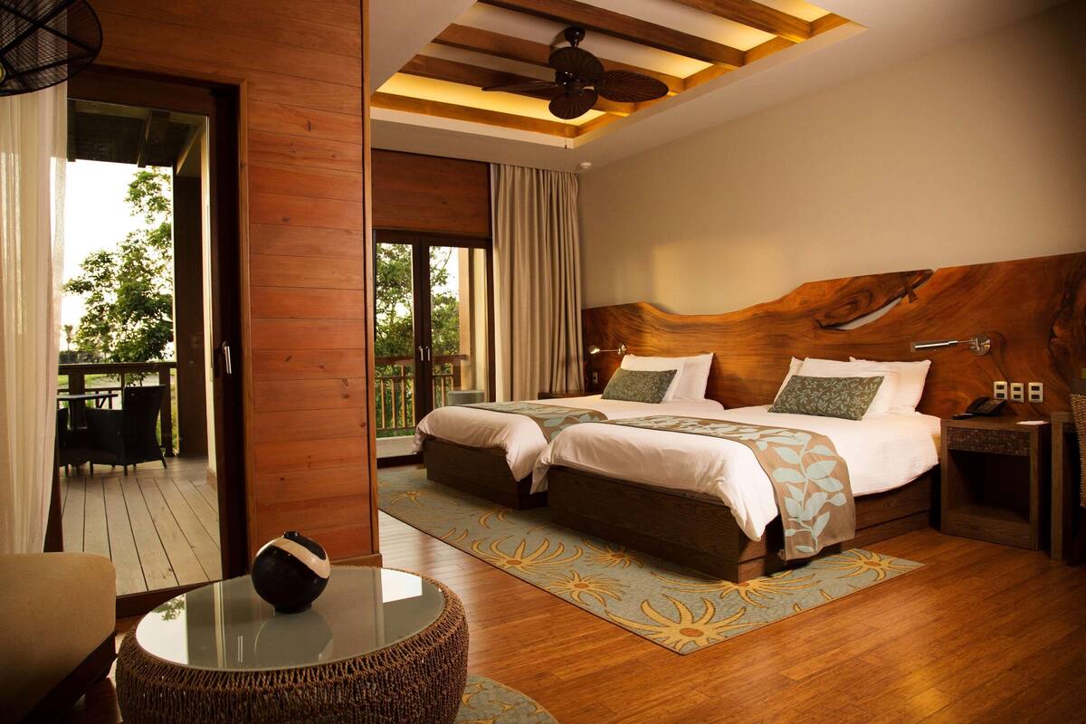 Un dormitorio con una cama grande, una mesita de vidrio, una silla de mimbre y vistas al exterior.