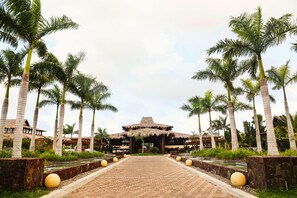 A pathway leading to a building with a thatched roof, flanked by palm trees and a brick walkway. - Indura Beach & Golf Resort, Curio Collection (Tela)