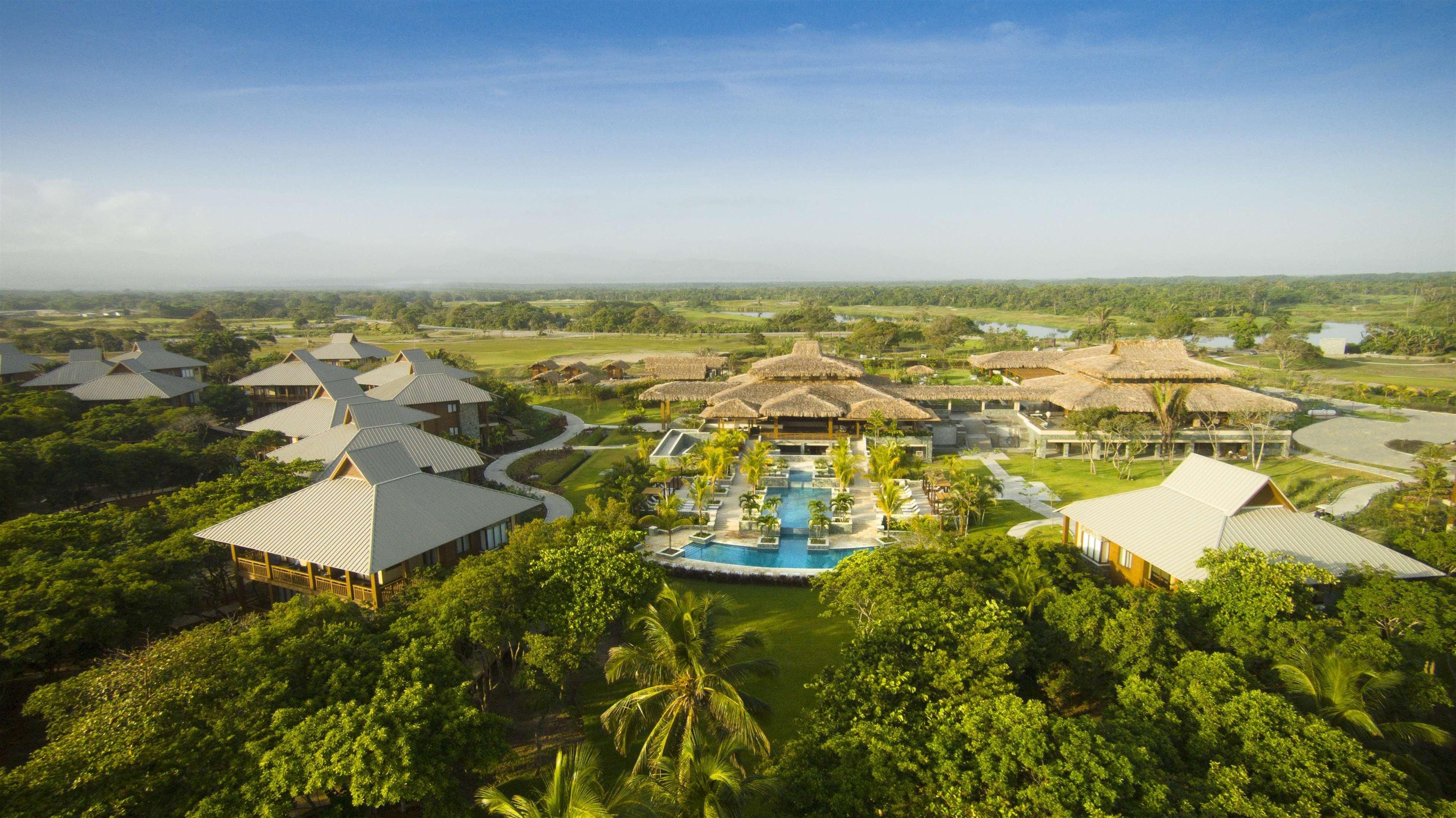 A resort with multiple bungalow-style buildings, a central pool, and surrounding lush greenery.