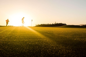 A golf course with a flagstick and players in silhouette against a sunset.