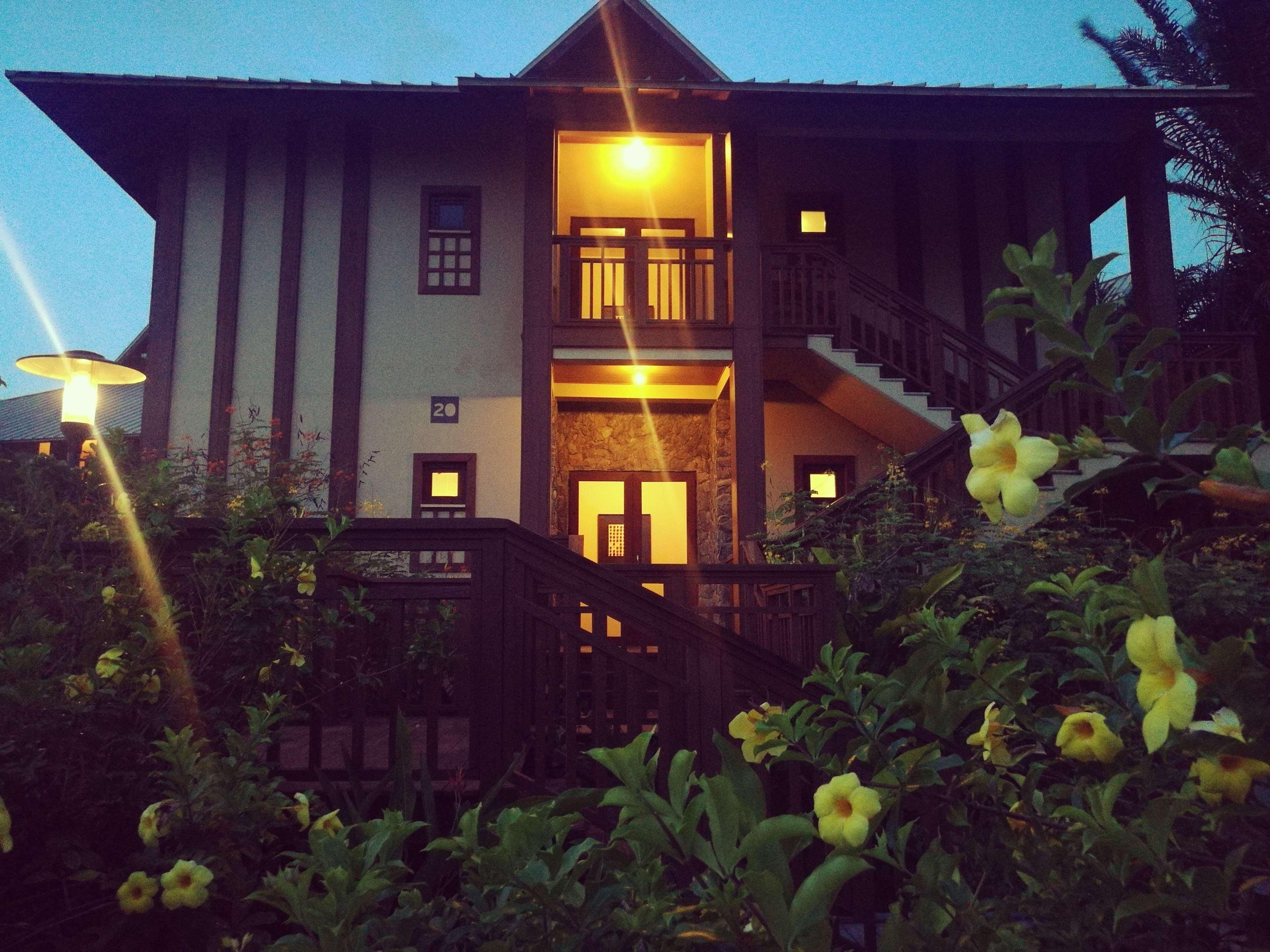 A two-story building with a staircase leading to the upper floor, surrounded by greenery.