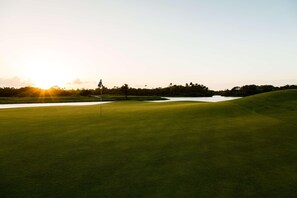 A golf course with a flag, water hazard, and trees in the background. - Indura Beach & Golf Resort, Curio Collection (Tela)