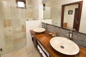Un baño con cabina de ducha de vidrio, dos lavamanos con lavabos redondos y un espejo grande sobre el mueble.