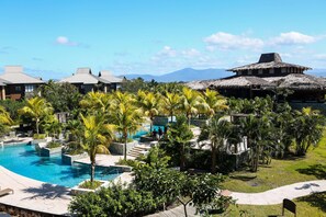 A resort with a swimming pool, palm trees, and a mountain view. - Indura Beach & Golf Resort, Curio Collection (Tela)