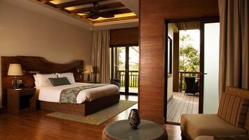 A hotel room with a large bed, a round coffee table, a sofa, and a balcony with outdoor furniture.